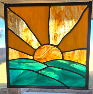 stained glass art showing the sunrise over green hills